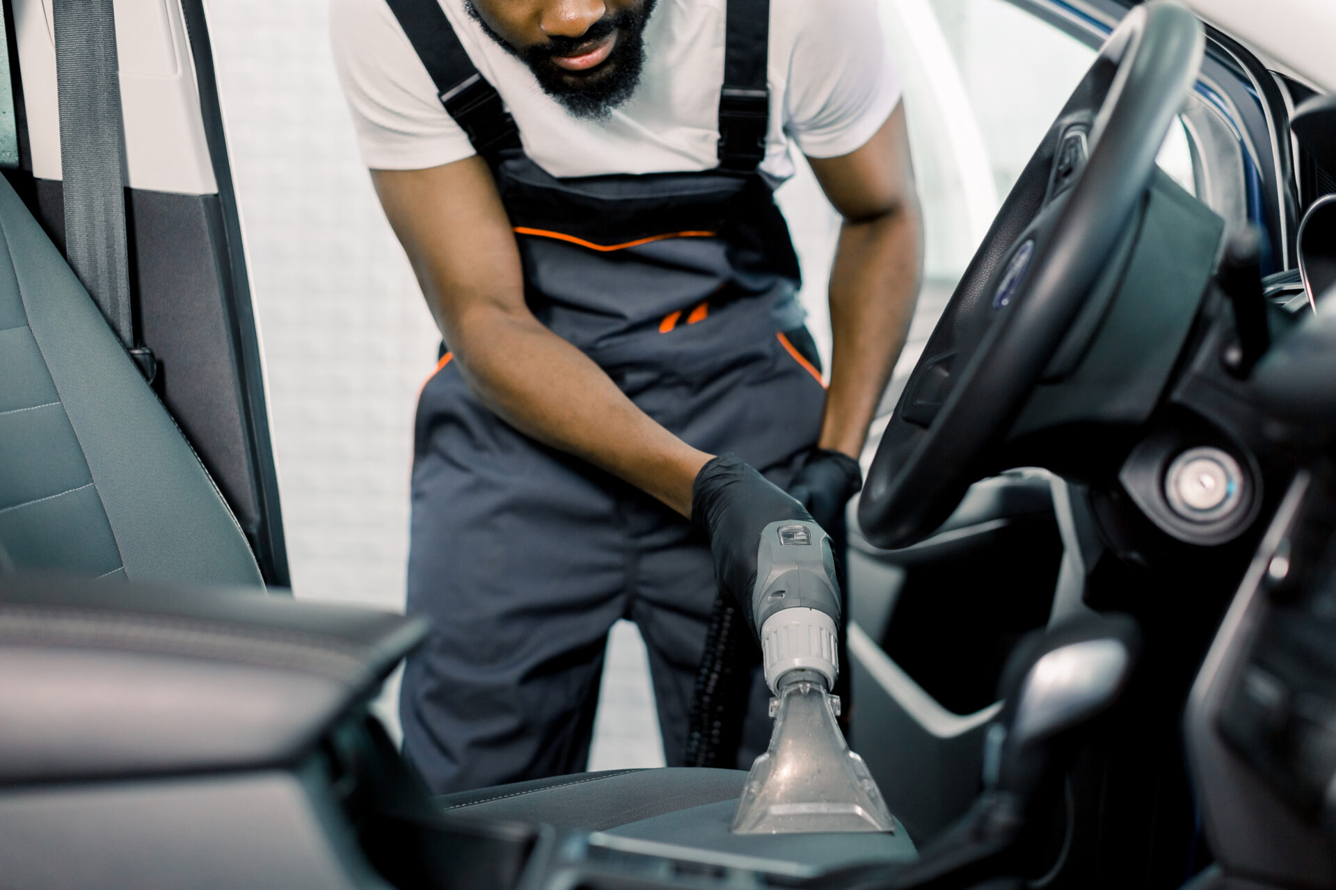 details of car vacuum cleaning. african professional male worker using wet vacuum cleaner for dirty car interior. auto car service cleaning the drivers seat, cleaning and vacuuming leather