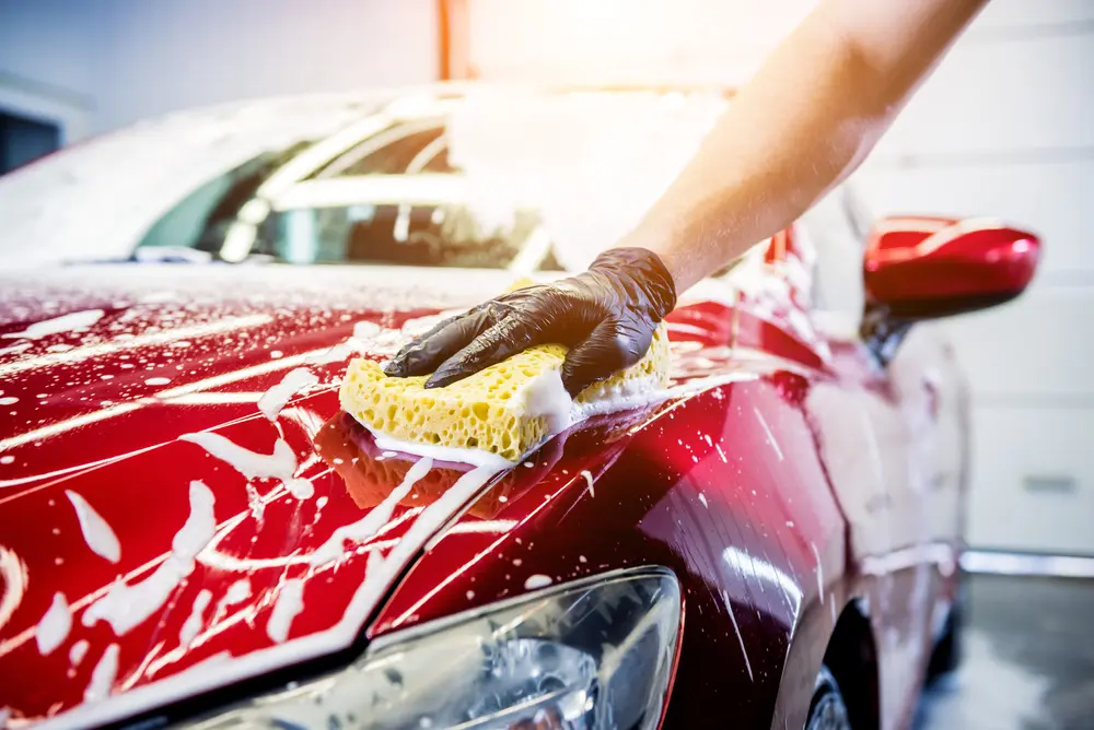 worker,washing,red,car,with,sponge,on,a,car,wash