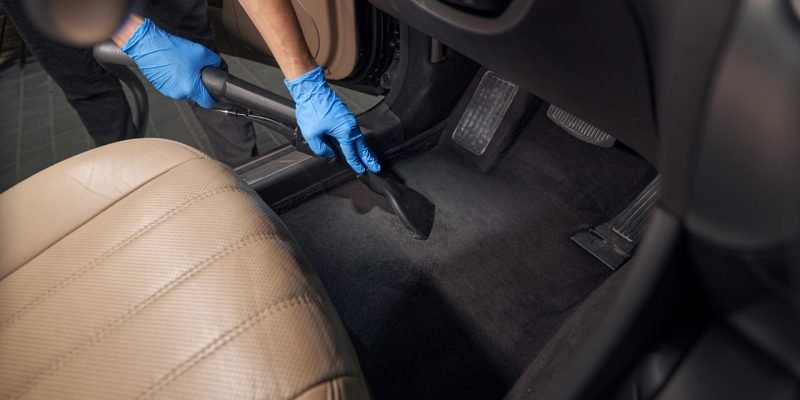 worker cleans car interior with vacuum cleaner